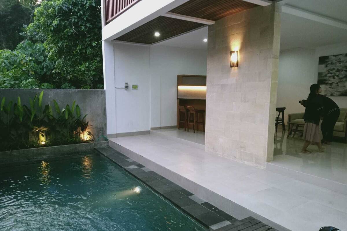 Un espace piscine extérieur moderne doté d’une terrasse en bois, d’un coin salon et d’un mur en pierre.