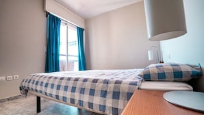 Een hotelkamer met een bed, een bureau, een lamp en een raam met gordijnen.