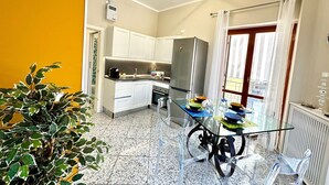 Cuina compacta amb armaris blancs, un frigorífic d'acer inoxidable i una taula de dinar de vidre amb caires transparents.