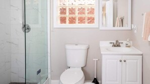 Une salle de bain avec une douche à parois de verre, des toilettes, un lavabo avec un miroir et une fenêtre donnant sur l’extérieur.