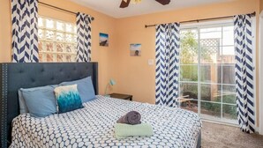 Une chambre à coucher avec un lit, un ventilateur de plafond et une vue sur l’extérieur grâce à une porte-fenêtre coulissante.
