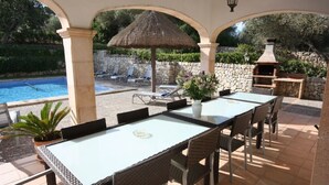 Un patio techado con piscina, sillas de descanso, una mesa con sillas, una parrilla y un florero.