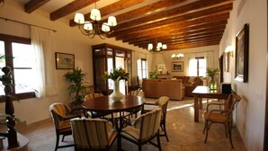 Un comedor amplio con una mesa y sillas de madera, una araña y vista al salón.