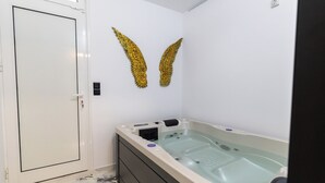 A spa room with a large bathtub, a door, and two golden wing decorations on the wall. - Apartment with jacuzzi and sauna.Fully furnished with kitchen absolutely private (Katie patisia)