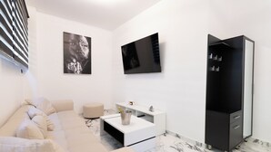 A modern living room with a beige sofa, a white side table with a TV, and a black cabinet. - Apartment with jacuzzi and sauna.Fully furnished with kitchen absolutely private (Katie patisia)