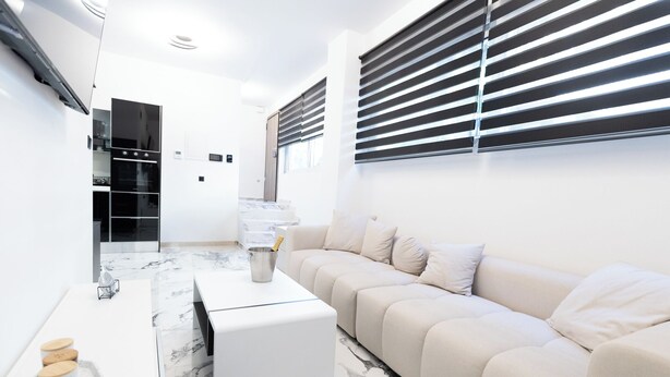A modern living room with a beige sofa, a white coffee table, and a marble-patterned floor. - Apartment with jacuzzi and sauna.Fully furnished with kitchen absolutely private (Katie patisia)