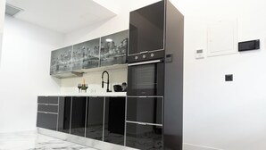 A modern kitchen with a black and white color scheme, featuring a built-in oven, a wine bottle, and a cityscape artwork on the wall. - Apartment with jacuzzi and sauna.Fully furnished with kitchen absolutely private (Katie patisia)