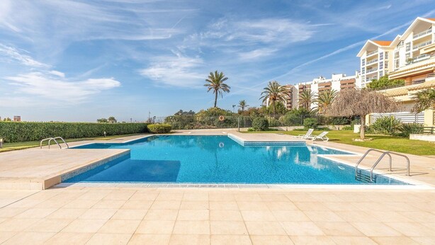 A swimming pool with a tiled deck, surrounded by palm trees and a building with balconies.