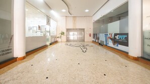 A clean, modern lobby with a marble floor, glass walls, and a central elevator.