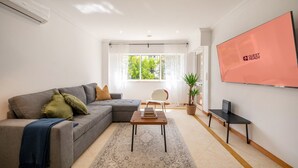 A modern living room with a grey sofa, a coffee table, a potted plant, and a large screen displaying "GUEST READY".