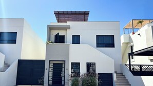A modern two-story building with a flat roof, a covered outdoor area, and a staircase leading to the upper level.