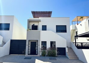 Enter through the black door and ascend the stairs to a shaded outdoor space under a pergola.