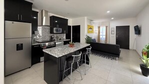 A modern kitchen with a central island, black cabinets, stainless steel appliances, and a dining area with a black sofa and bar stools.