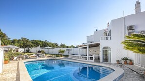 A swimming pool surrounded by a white building with a stone patio, outdoor furniture, and potted plants. - Comfortable Villa in Carvoeiro, Algarve (Carvoeiro)