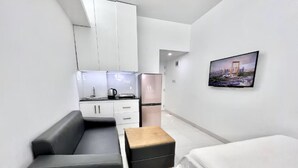 Una habitación moderna con cama, sofá, una pequeña mesa, zona de cocina y televisor montado en la pared.