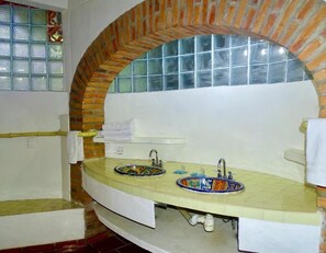 Une salle de bain dotée d’un meuble-lavabo aux lignes courbes, de deux vasques ornées de carreaux décoratifs, d’une fenêtre avec du verre teinté en bleu et d’une arche en briques.
