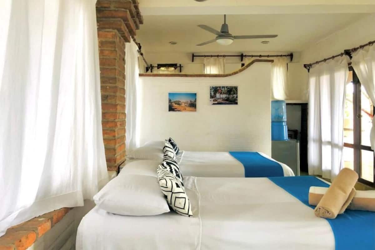Habitación de hotel con dos camas, un ventilador de techo y una pared de ladrillo.
