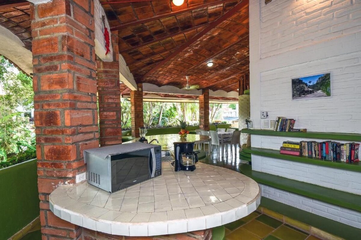 A covered outdoor area with a brick column, a microwave, a coffee maker, and a bookshelf with books.
