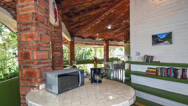 A covered outdoor area with a brick column, a microwave, a coffee maker, and a bookshelf with books. - Jardin De Playa Sayulita (Sayulita)