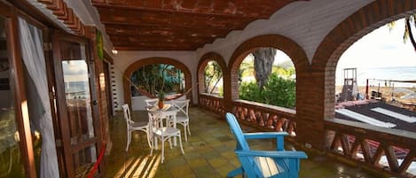 A covered patio with a table and chairs, a blue chair, and a bowl of fruit on a table.