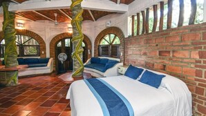 A room with a brick wall, a bed with blue pillows, a bench, and a fan. - Jardin De Playa Sayulita (Sayulita)