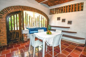 A room with a white brick wall, a wooden door, a blue sofa, a white table with a pineapple and fruit, and a tiled floor. - Jardin De Playa Sayulita (Sayulita)