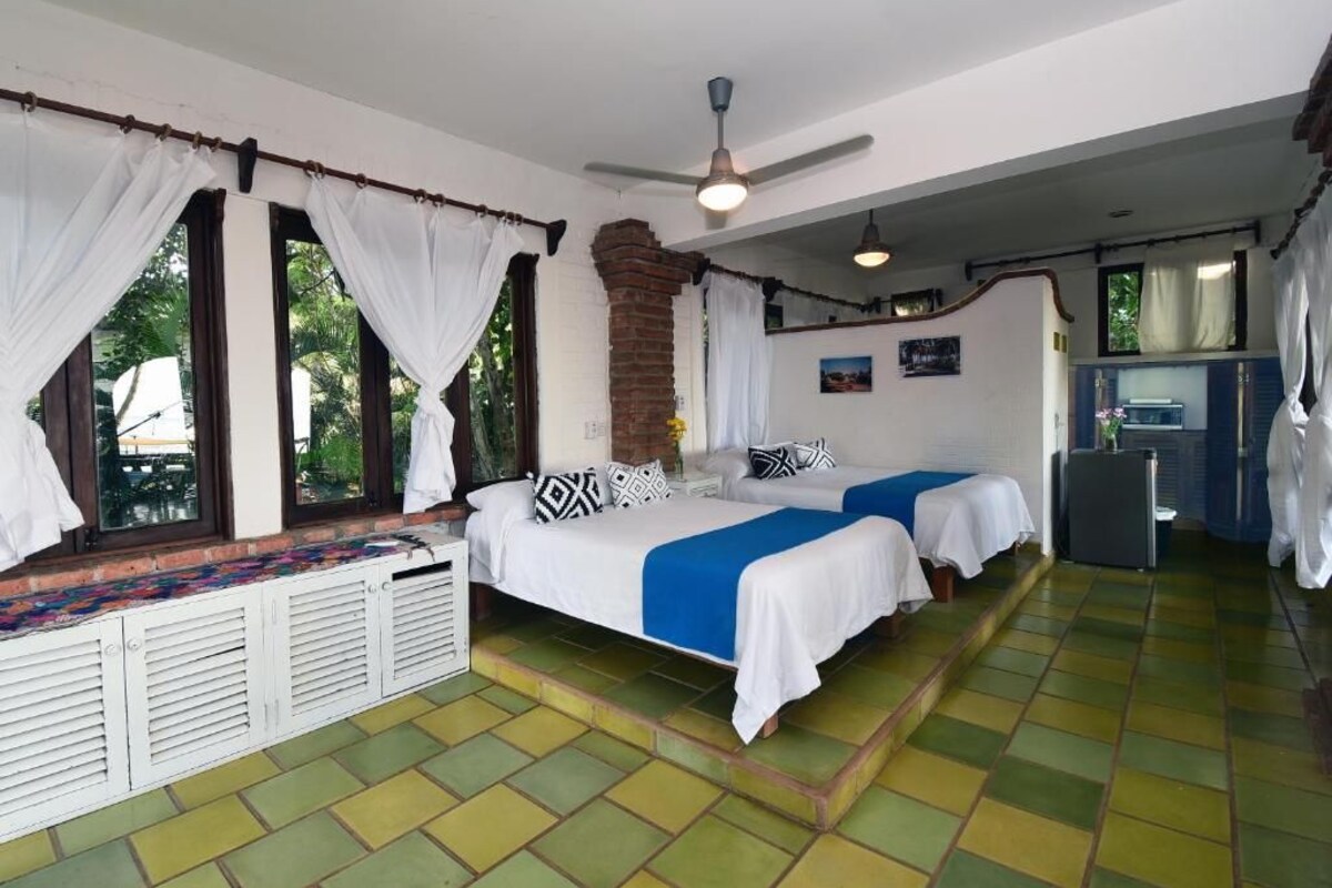 A room with two beds, a ceiling fan, and a small kitchenette.