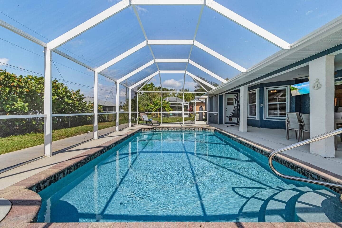 A swimming pool with a covered area, surrounded by a white fence, and a building with outdoor seating.