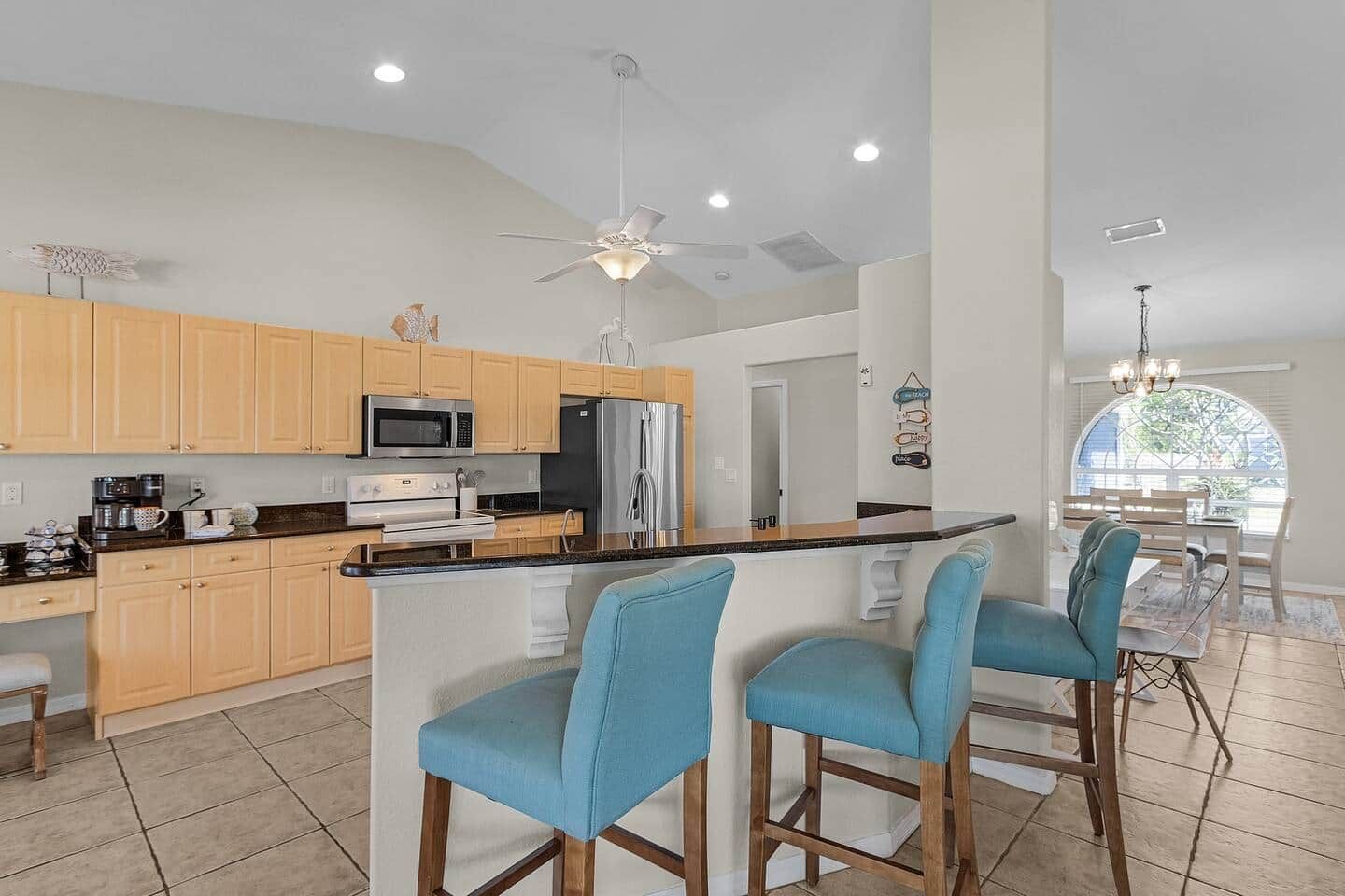 A modern kitchen with wooden cabinets, a stainless steel refrigerator, and a bar area with blue chairs.