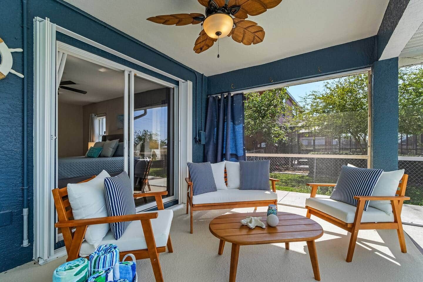 Un balcon doté d’un ventilateur de plafond, de chaises en bois avec des coussins à rayures, d’une table ronde et d’une vue sur l’extérieur.