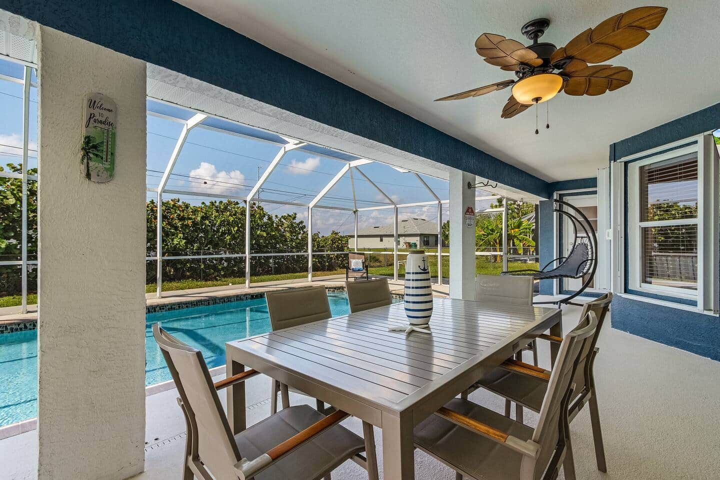 A covered outdoor area with a pool, a table with chairs, and a ceiling fan.