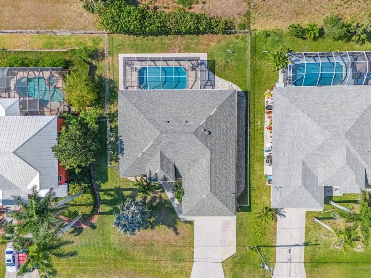 An aerial view of a residential area with two houses, each featuring a swimming pool and a distinct geometric roof design.