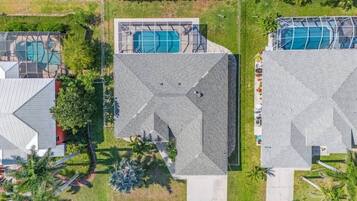 An aerial view of a residential area with two houses, each featuring a swimming pool and a distinct geometric roof design.