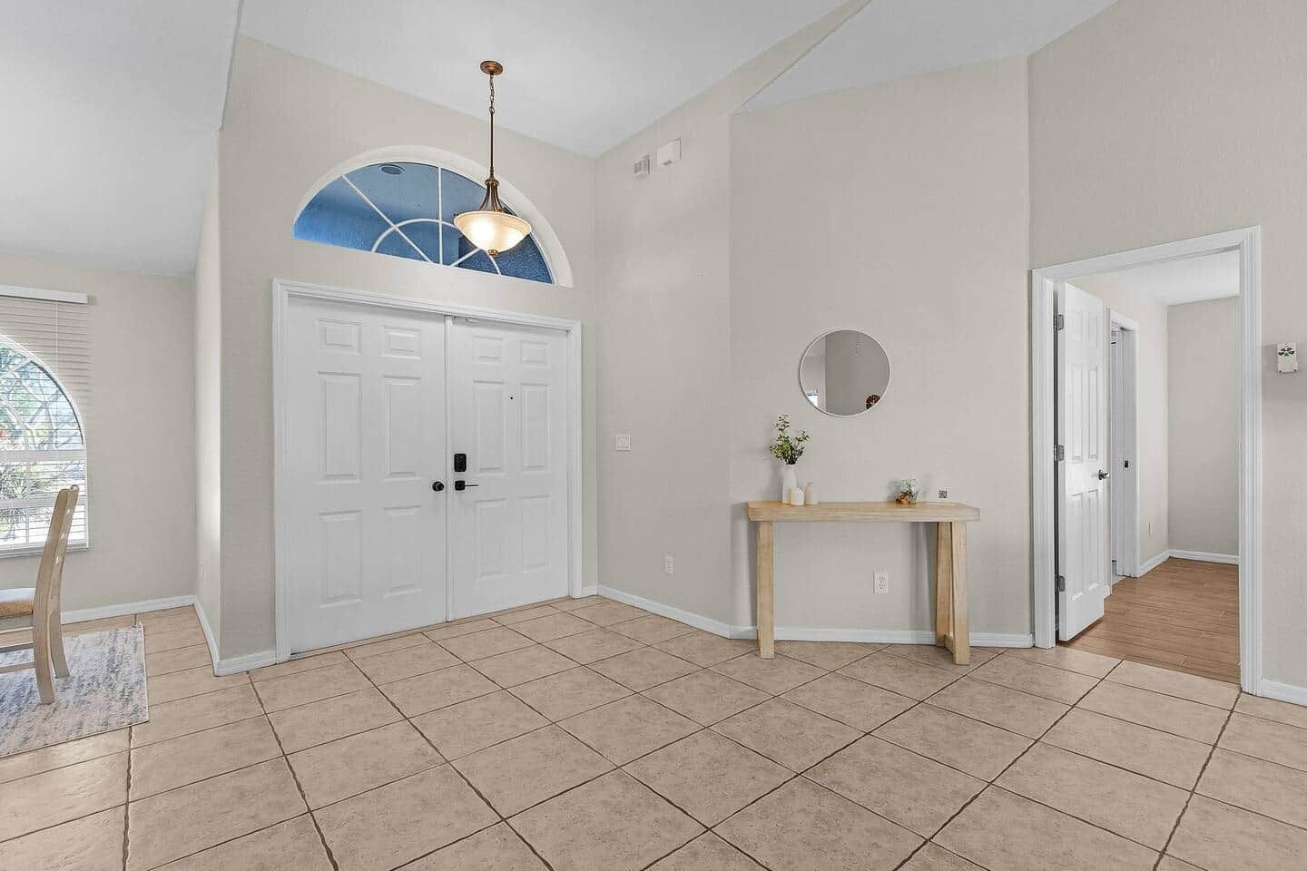A spacious room with a large arched window, a wooden console table with a mirror, and a white door.