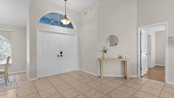 A spacious room with a large arched window, a wooden console table with a mirror, and a white door.