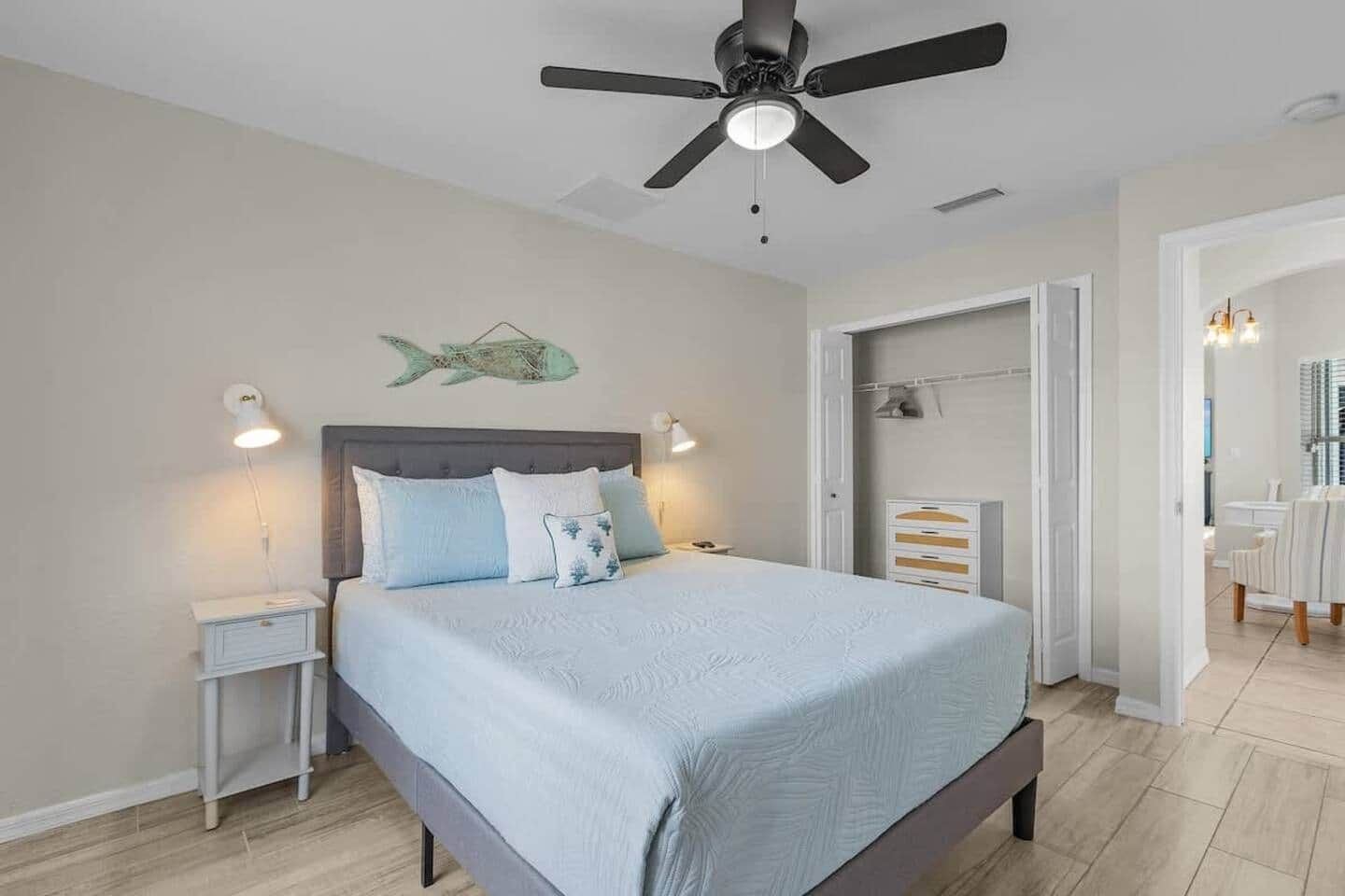 A bedroom with a bed, nightstands, a ceiling fan, and a fish wall decoration.