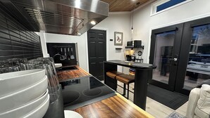Una cocina moderna con encimera negra, electrodomésticos de acero inoxidable y un salpicadero de madera. Hay una zona de comedor con un banco y una mesa pequeña.