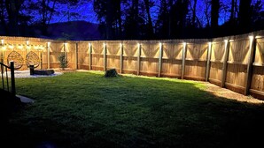 Un patio trasero cercado con un área de patio bien iluminada, un pequeño jardín y una valla de madera.