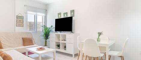 Una sala de estar moderna con sofá, mesa de centro, televisor y comedor con sillas y una mesita.