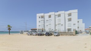 A multi-story building with balconies, a parking area with cars, and a beach in the background. - Beachfront Apartment with Sea Views in Barbate (Barbate)