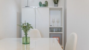 A white table with a green vase, a white chair, a white cabinet with a shelf, and a small potted plant. - Beachfront Apartment with Sea Views in Barbate (Barbate)