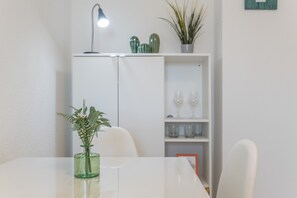 Una mesa blanca con un florero verde, una silla blanca, un mueble blanco con estante y una pequeña planta en maceta.
