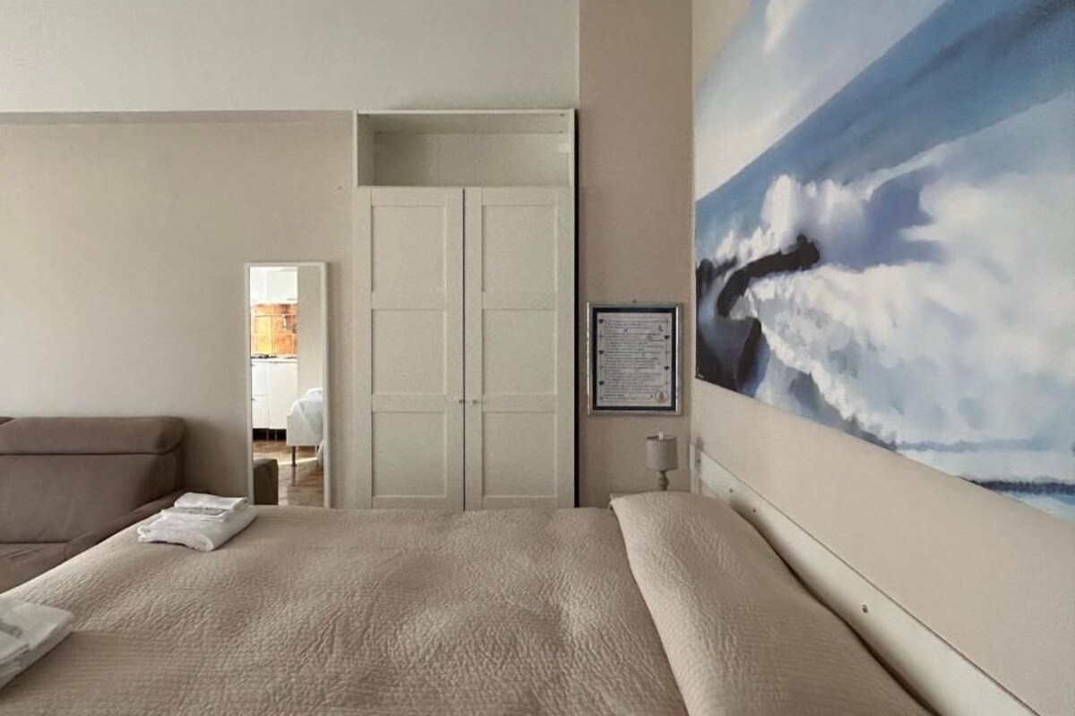 A hotel room with a large bed, a painting of clouds on the wall, and a view into the bathroom.