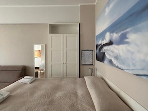 A hotel room with a large bed, a painting of clouds on the wall, and a view into the bathroom. - Monolocali Da Vinci (Falconara Marittima)
