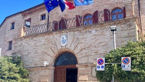 A historic building with a brick facade, a central entrance with a wooden door, and multiple flags including the EU flag. - Monolocali Da Vinci (Falconara Marittima)
