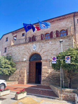 Un edificio histórico con una entrada destacada, banderas y señales de prohibido estacionar.