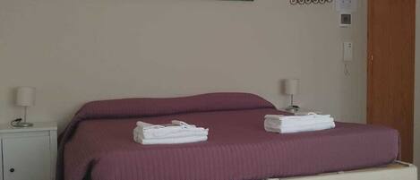 A bedroom with a bed, two bedside tables, a wall-mounted light fixture, a decorative wall piece, and a patterned floor.