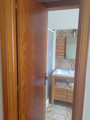 A wooden door leading to a bathroom with a tiled floor, a sink, and a mirror.