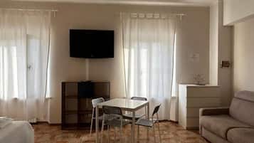 Una camera d'albergo con un letto, un divano, un tavolo da pranzo con sedie, una TV fissata al muro e un piccolo mobile.