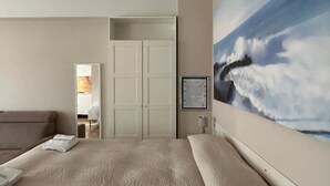 A hotel room with a large bed, a painting of clouds on the wall, and a view into the bathroom. - Monolocali Da Vinci (Falconara Marittima)